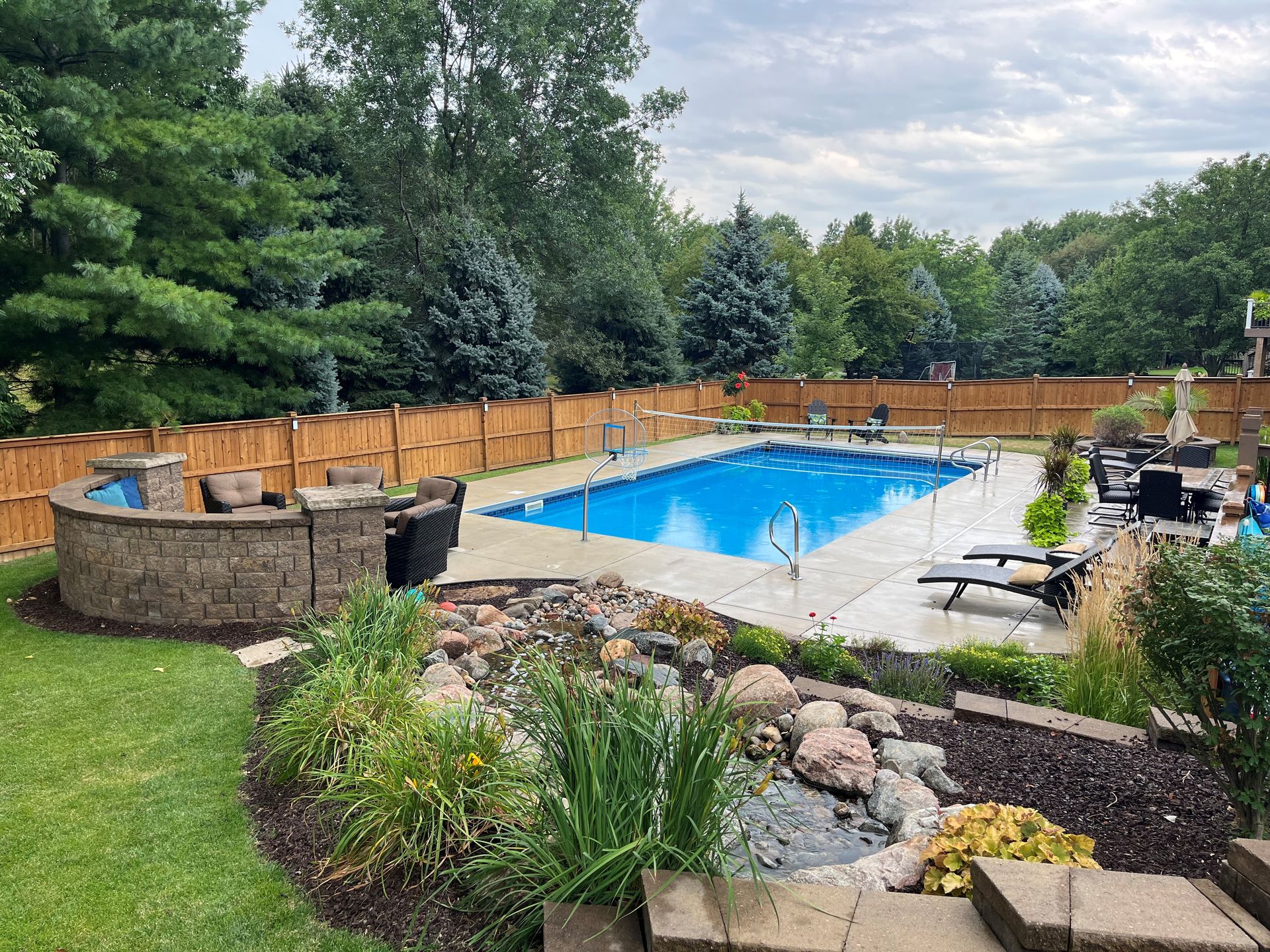 One of Olympic Pool & Spa's inground builds: a fenced Omaha backyard pool with a volleyball net and lounge chairs