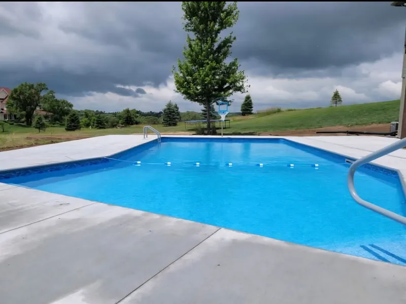 Rectangular inground pool with a basketball hoop and a float line on an acreage under a storm sky, built by Olympic Pool & Spa in the Omaha metro